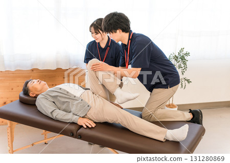 A senior man receiving massage and stretching during rehabilitation, and male staff including a physical therapist and occupational therapist 131280869