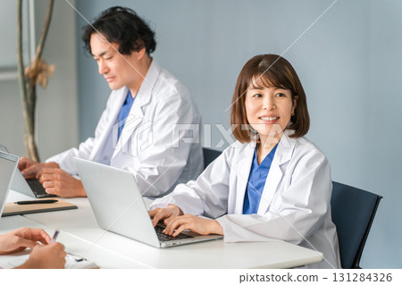 Male and female doctors in white coats sitting at desks and working 131284326