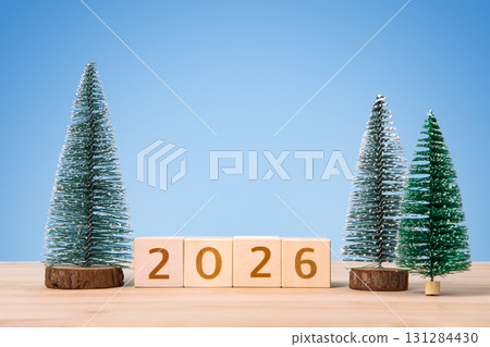 New Year 2026 and Christmas postcard. Wooden cubes with numbers 2026 and green Christmas trees on a wooden table and a blue background. New Year 2026 and Christmas postcard. Wooden cubes with numbers 2026 and green Christmas trees on a wooden table and a blue background. 131284430