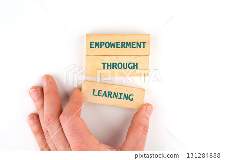 Through education and learning to success concept. EMPOWERMENT THROUGH LEARNING words made from blocks by hand on a light background, top view 131284888