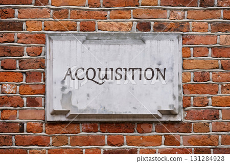 Corporate acquisition and merger concept. Copy space. ACQUISITION text written on a plaque on a weathered brick wall. 131284928