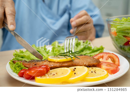 Asian elderly woman patient eating salmon stake and vegetable salad for healthy food in hospital. 131284985