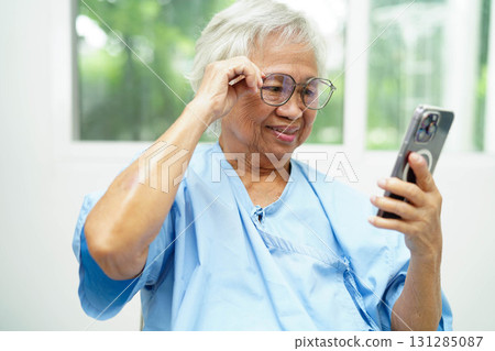 Asian senior woman wearing eyeglasses or vision glasses using a smartphone at home care service. 131285087