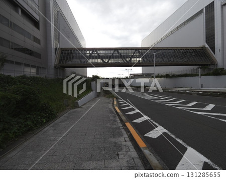 A wide roadway and an impersonal space beneath the walkway connecting two huge buildings 131285655