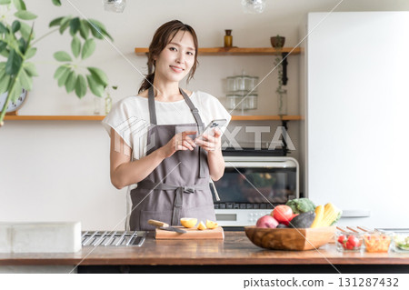 Asian woman using smartphone app in home kitchen/dining Asian woman using smartphone app in home kitchen/dining 131287432