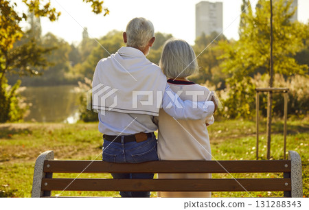 Back view of mature senior couple family sitting on the bench in park and hugging Back view of mature senior couple family sitting on the bench in park and hugging 131288343