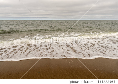 Ocean waves reaching sandy shore under cloudy sky Ocean waves reaching sandy shore under cloudy sky 131288561