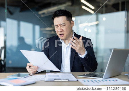 Angry young Asian man received a letter and bad news, sitting disappointed in the office, reading and holding documents in his hands. Angry young Asian man received a letter and bad news, sitting disappointed in the office, reading and holding documents in his hands. 131289468
