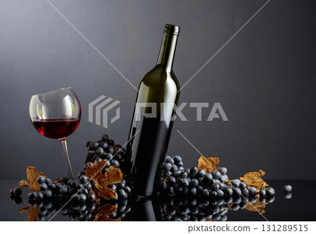 Bottle and glass of red wine with blue grapes on a black background. 131289515