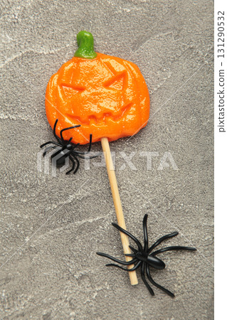 Halloween lollipops shaped like a pumpkin with decorative spider on grey concrete background. Vertical photo 131290532