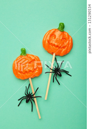 Halloween lollipops shaped like a pumpkin with decorative spider on mint background. Vertical photo Halloween lollipops shaped like a pumpkin with decorative spider on mint background. Vertical photo 131290534