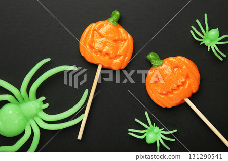 Halloween lollipops shaped like a pumpkin with decorative spider on black background. 131290541