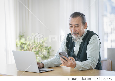 Senior man looking at smartphone while working on laptop 131290869