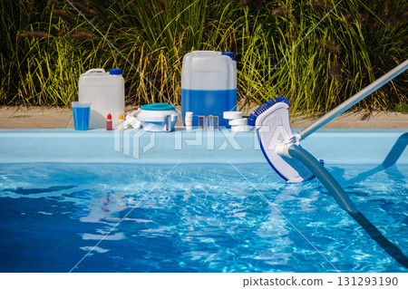 Swimming pool cleaning in process with vacuum brush and hose in water, maintenance products including chemical canisters, chlorine tablets, dispenser and test kit on poolside Swimming pool cleaning in process with vacuum brush and hose in water, maintenance products including chemical canisters, chlorine tablets, dispenser and test kit on poolside 131293190