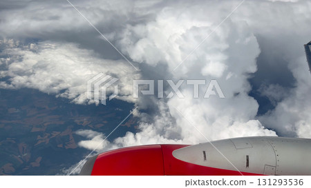 Wing of an airplane above white fluffy clouds in the blue sky. 131293536