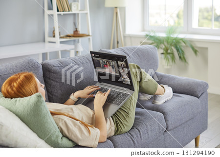 Young redhead woman lying on sofa at home having online video call with colleague or a friend 131294190