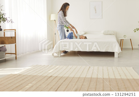 Mother holding hands of her happy little daughter who is lying on the bed at home Mother holding hands of her happy little daughter who is lying on the bed at home 131294251