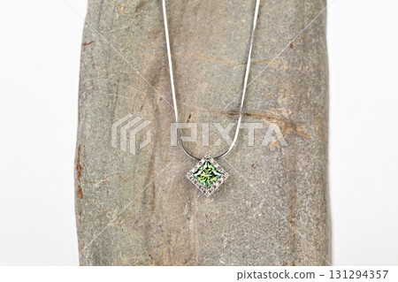 A green gemstone pendant is displayed on a rock A green gemstone pendant is displayed on a rock 131294357