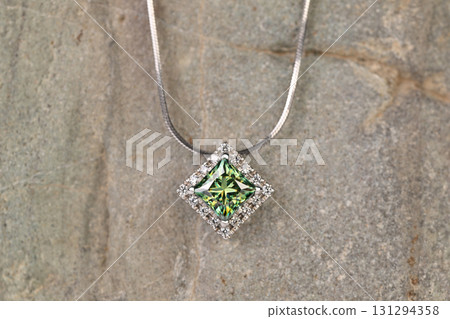 A green and white diamond shaped pendant is on a stone surface A green and white diamond shaped pendant is on a stone surface 131294358