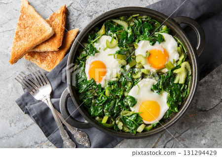 Green shakshuka is a stew of eggs in a mixture of green vegetables and herbs, close-up in a frying pan. Horizontal top view Green shakshuka is a stew of eggs in a mixture of green vegetables and herbs, close-up in a frying pan. Horizontal top view 131294429