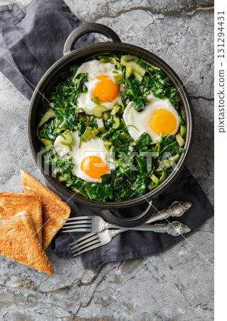 Green shakshuka is a stew of eggs in a mixture of greens, herbs and other vegetables such as spinach, celery, peppers and green onions close-up. Vertical top view Green shakshuka is a stew of eggs in a mixture of greens, herbs and other vegetables such as spinach, celery, peppers and green onions close-up. Vertical top view 131294431