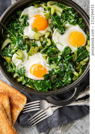 Healthy green shakshuka with eggs, spinach, celery, onion, green pepper and herbs close-up in a frying pan on the table. Vertical top view Healthy green shakshuka with eggs, spinach, celery, onion, green pepper and herbs close-up in a frying pan on the table. Vertical top view 131294433