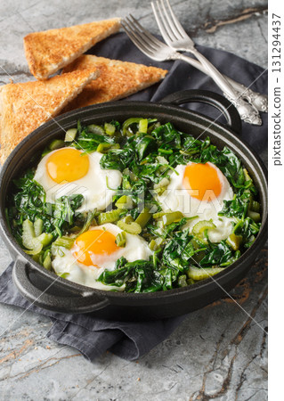 Green shakshuka is a stew of eggs in a mixture of greens, herbs and other vegetables such as spinach, celery, peppers and green onions close-up in a frying pan. Vertical Green shakshuka is a stew of eggs in a mixture of greens, herbs and other vegetables such as spinach, celery, peppers and green onions close-up in a frying pan. Vertical 131294437
