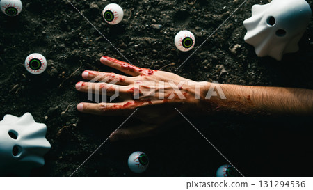 Bloody hand surrounded by plastic eyeballs and ghost figurines on dirt. 131294536