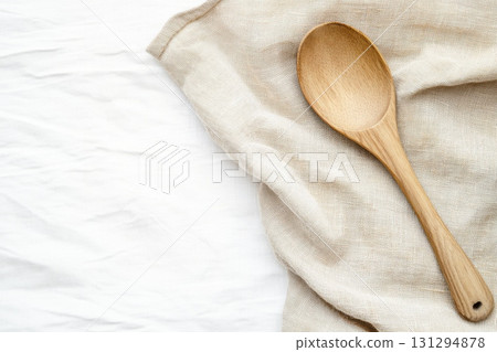 Wooden kitchen spoon placed diagonally on grain sack linen cloth, isolated on white background with warm rustic tones and farmcore simplicity 131294878