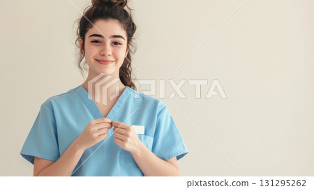 Minimalistic scene of healthcare worker in blue scrubs adding thank-you badge, expressing appreciation and professionalism, ideal for medical campaigns and recognition visuals. 131295262