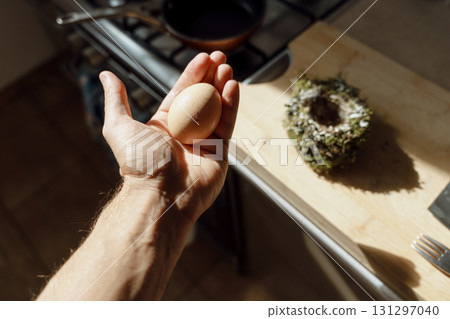 A chicken egg in a hand. A bird's nest in the table at the background. Kitchen interior.  131297040