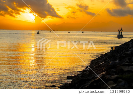 Tranquil dawn seascape. Beautiful sunrise over the sea, featuring traditional fishing boats catching the first light. Tranquil dawn seascape. Beautiful sunrise over the sea, featuring traditional fishing boats catching the first light. 131299980