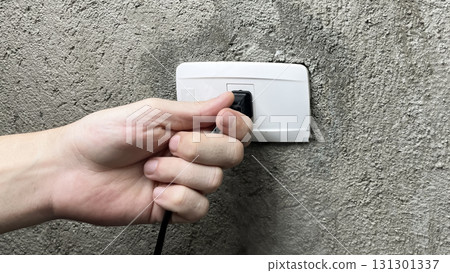 a hand pulling the plug out of an outlet 131301337
