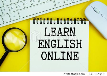 Notepad with the text "Learn English Online" and white keyboard, wireless mouse, magnifying glass on yellow background 131302348