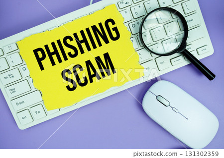 Yellow torn paper with the text "Phishing Scam" placed on a white keyboard, and magnifying glass and a computer mouse Yellow torn paper with the text "Phishing Scam" placed on a white keyboard, and magnifying glass and a computer mouse 131302359