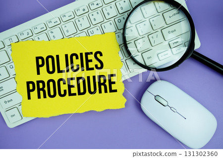 Yellow torn paper with the text "Policies Procedure" placed on a white keyboard, and magnifying glass and a computer mouse 131302360