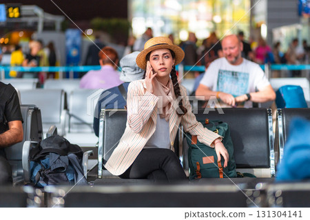Young Caucasian woman, elegantly dressed, is sitting on chairs at the airport or train station. Woman using smartphone and calls. The concept of travel and vacation Young Caucasian woman, elegantly dressed, is sitting on chairs at the airport or train station. Woman using smartphone and calls. The concept of travel and vacation 131304141