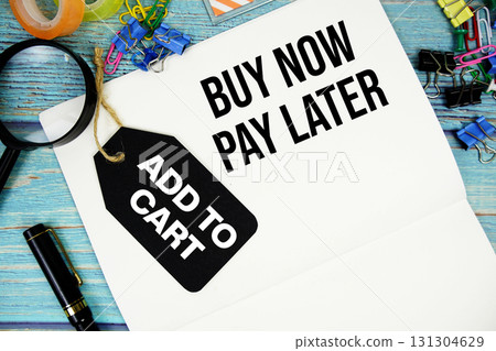 Buy Now Pay Later text on a notepad paper and Add to cart with price tag surrounded by office supplies and magnifying glass on a blue wooden surface 131304629