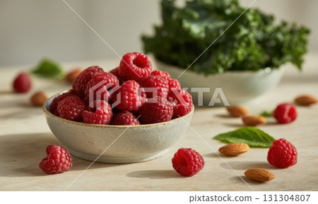 Light ceramic bowl overflowing with fresh, vibrant raspberries, almonds, and kale on a table Light ceramic bowl overflowing with fresh, vibrant raspberries, almonds, and kale on a table 131304807