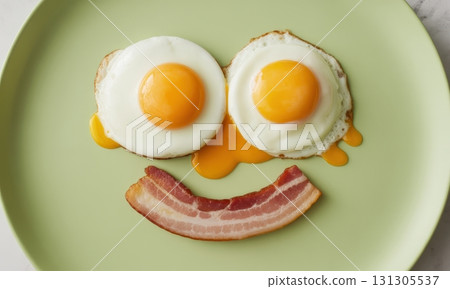 Sunny side up eggs and bacon strip arranged as a happy smiley face on a green plate 131305537