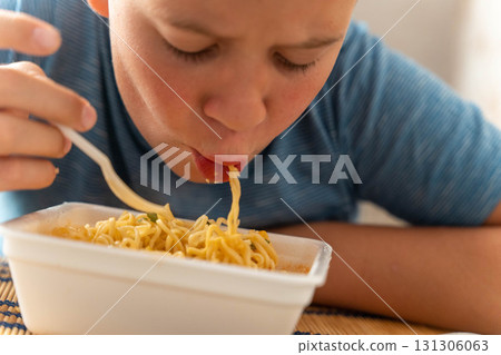 Boy eating instant noodles with fork from container Boy eating instant noodles with fork from container 131306063