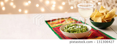 Cinco de Mayo table with guacamole, tortilla chips, festive drink in vibrant setting 131306427