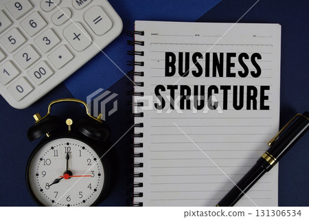 Business Structure text written on notepad with calculator and alarm clock on navy blue background Business Structure text written on notepad with calculator and alarm clock on navy blue background 131306534