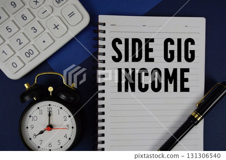 Side Gig Income text written on notepad with calculator and alarm clock on navy blue background Side Gig Income text written on notepad with calculator and alarm clock on navy blue background 131306540