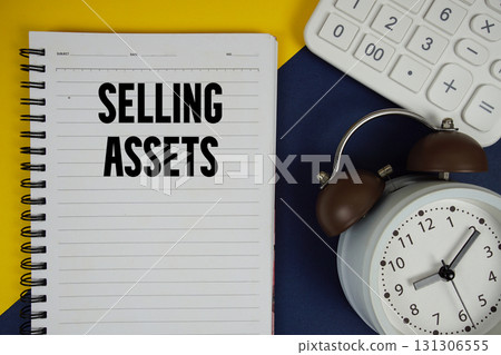 Selling Assets text written on notepad with calculator and alarm clock on navy blue background 131306555