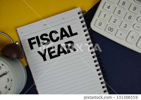 Fiscal Year text written on notepad with calculator and alarm clock on navy blue background 131306559