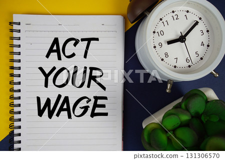 Act Your Wage text written on notepad with alarm clock on yellow and navy blue background 131306570