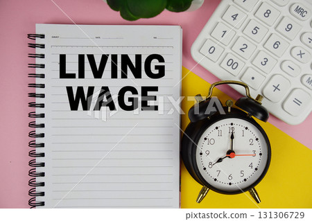 Living Wage text written on notepad with calculator and alarm clock on pink background 131306729
