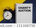 Charity Auction text written on notepad with alarm clock on yellow background 131306736