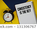 Consistency Is The Key text written on notepad with alarm clock on yellow background 131306767
